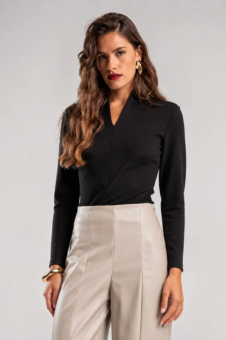 Teta Arvanitaki Ginger Black Blouse, front view showing the V-neckline, padded shoulders and geometric seams, styled with cream trousers.